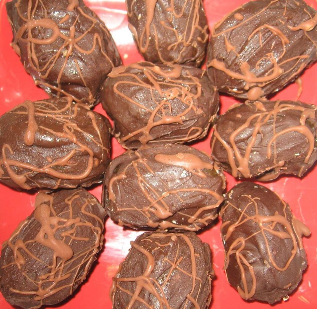 A red plate showcases chocolate-covered dates elegantly arranged in a circle. These plant-based treats are drizzled with more chocolate, creating an appetizing, textured appearance perfect for any vegan indulgence.