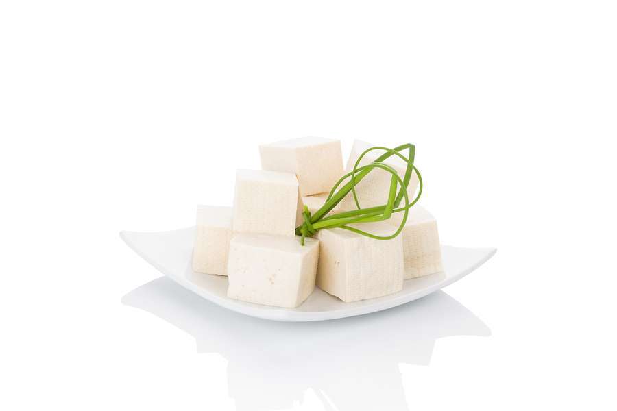 A plate of cubed tofu neatly stacked, tied together with a sprig of green onion, embodies the essence of a vegan lifestyle on a white background.